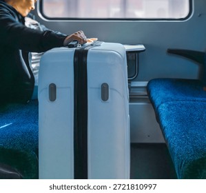 Horizontal wide angle eye level shot showing a rolling luggage placed in the legroom area between fabric passenger seats inside a commuter train