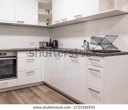 Horizontal wide angle eye level shot of a clean L-shaped kitchen featuring white glossy cupboards, built-in oven, and a wooden floor in a studio