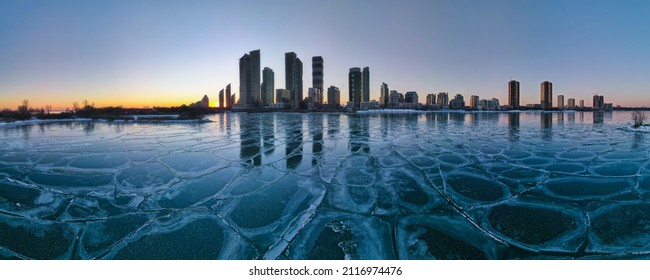 Horizontal Wide Angle Large Panorama Of Frozen Lake With Toronto Etobicoke Neighborhood City Skyline With Highrise Condo Buildings In The Background Shot At Sunset Hour.