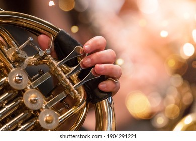 Horn professional player with symphony orchestra performing in concert on background.