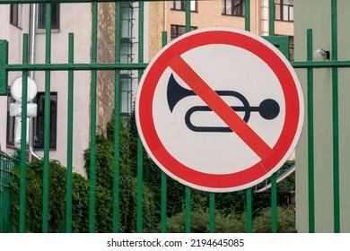 Horn prohibited road sign mounted on green fence. Buildings in background. - Shutterstock ID 2194645085