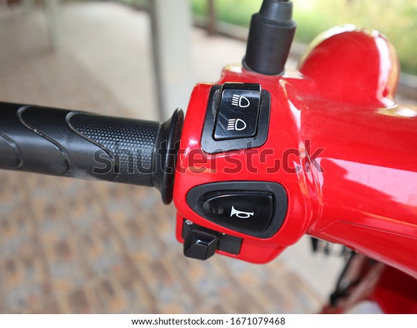 Horn switch and light switch on a red\
motorcycle handlebar.