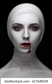 Horrible and Halloween theme: portrait of a young girl model with bandages on her head and blood on her face on a dark background in the studio with bloody hands, bloody make-up