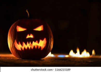 Horrible symbol of Halloween - Jack-o-lantern. Scary head of pumpkin in hell fire flames. Half of orange gourd on the left side. Glowing face, trick or treat. Copy Space.