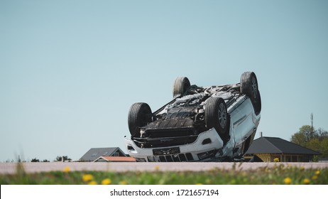 Horrific Traffic Accident Rollover Smoking And Burning Vehicle Lying On Its Roof In The Middle Of The Road After Collision. Daytime Crash Scene With Damaged Car. Low Angle Shot