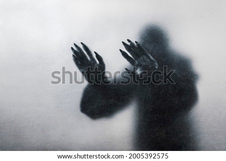 Horrifiying figure with long claws behind a dusty scratched glass
