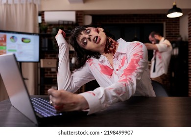 Horror Cruel Zombie Using Laptop At Desk, Undead Corpse Trying To Work On Computer In Startup Office. Creepy Aggressive Brain Eating Monster Looking Terrifying And Horrible, Sinister Danger.