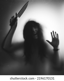 Horror, halloween background - Shadowy figure behind glass holding a knife - Shutterstock ID 2196170131