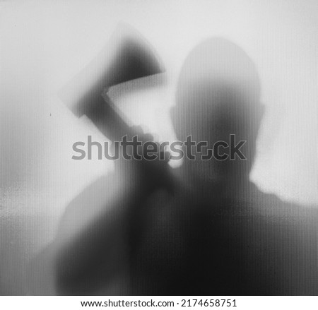 Horror, halloween background - Shadowy figure behind glass of a man holding an axe