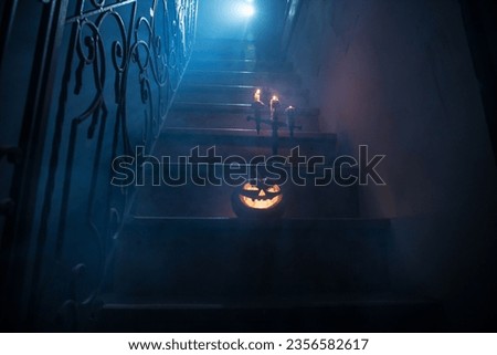 Horror Halloween concept. Creepy abandoned castle. An old candlestick and Halloween pumpkin glowing on wooden stairs with lattice door at night. Decoration with backlight and fog. Selective focus