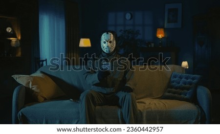 Horror maniac sitting on the sofa in the living room and holding smartphone, watching social media.