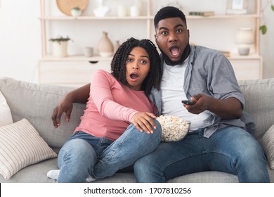 Horror Movie. Shoked black couple watching scary film on tv and eating popcorn at home, free space