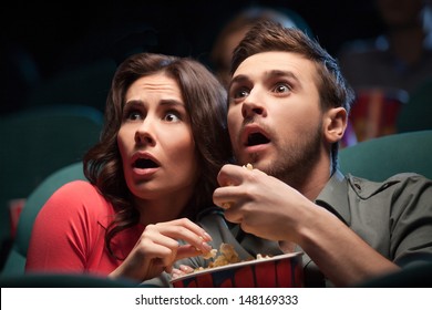 Horror movie. Terrified young couple eating popcorn while watching movie at the cinema - Powered by Shutterstock