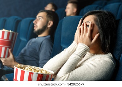 Horror Movies Are For Brave Ones. Closeup Shot Of A Scared Girl Closing Her Eyes With Her Hands Watching Scary Movie In The Cinema