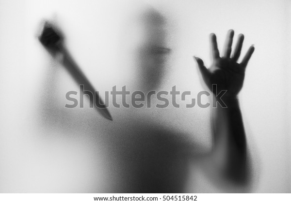 Horror Murderer. Dangerous man behind the frosted glass with a knife on his hand.Halloween background.Black and white picture