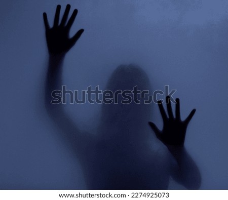 Horror, mystery and shadow of a woman on a window for fear, escape or nightmare. Dark, hands and a ghost, girl or person with paranormal activity, spooky behavior or strange movement in a studio