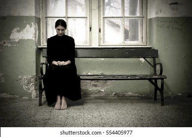 Horror scene of a scary woman. Woman in black dress sitting on the bench in demolished room