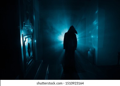 Horror Silhouette Of Ghost Inside Dark Room With Mirror. Scary Halloween Concept. Silhouette Of Witch Inside Haunted House With Fog And Light On Background. Selective Focus