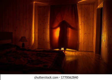 Horror Silhouette In Window With Curtain Inside Bedroom At Night. Horror Scene. Halloween Concept. Blurred Silhouette Of Ghost