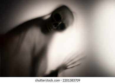 Horror Skeleton Or Grim Reaper Behind The Matte Glass. Halloween Festival Concept.Blurred Picture