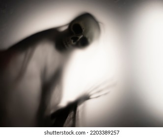 Horror Skeleton Or Grim Reaper Behind The Matte Glass. Halloween Festival Concept.Blurred Picture