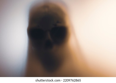 Horror Skeleton Or Grim Reaper Behind The Matte Glass. Halloween Festival Concept.Blurred Picture