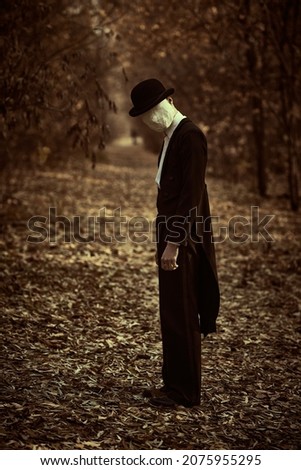 Horror, thriller. A strange and creepy gentleman in a mask of plaster bandage on his face, in a bowler hat and a black tailcoat, stands in an old autumn park. Halloween. Vintage style. 