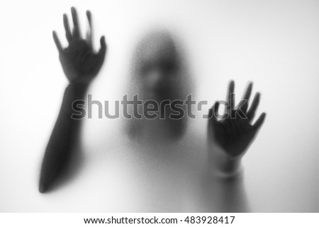 Horror woman behind the matte glass in black and white. Blurry hand and body figure abstraction.Halloween background