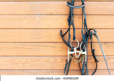 Horse bridle with decoration hanging on stable wooden wall. Front view. Closeup outdoors horizontal image with copy space.
