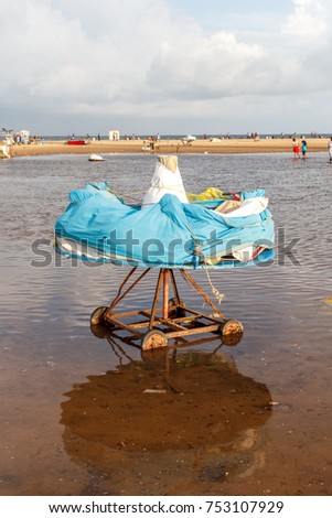 Horse or carousel swing ride covered to protect from rain seen at Marina beach, Chennai,India. Surrounded by rain water with dark clouds formed in the sky. Reflection of swing ride in water.