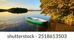 Horse Chestnut Tree by calm lake in full autumn colour at sunset and a rowing boat tied to a wooden pier