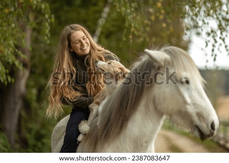 Horse and dog concept: A young female equestrian and her dog on her icelandic horse in front of a rural farm landscape