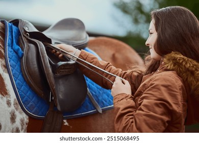 Horse, girl and adjust saddle outdoor for race, sport and training at countryside or farm. Animal, equestrian and prepare strap or gear for riding with pet for care with teenager at horseback school - Powered by Shutterstock