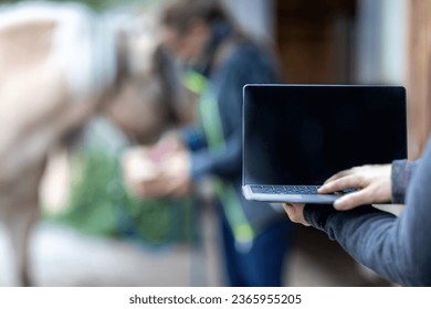 Horse owner as digital online clients: A laptop in front of blurred horse and owner paddock scene, consulting online advice and online shopping as horse owner - Powered by Shutterstock