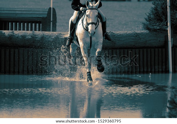 Horse\
and rider at a water jump competing, in the cross country stage, at\
an equestrian three day event. With colour\
toning