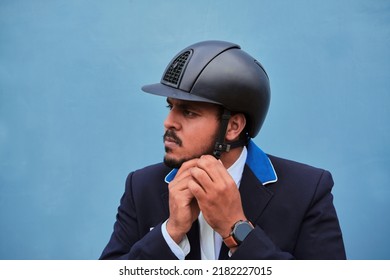 Horse rider wearing uniform fastening his helmet before competing, on a blue background