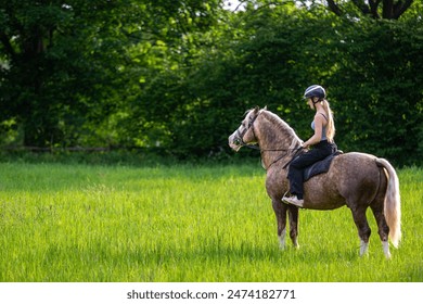 Horse riding in the meadow, Image shows a beautiful young girl in her 20's riding her section D Welsh cob palomino stallion admiring the scenery on a sunny day just as the sun begins to set - Powered by Shutterstock