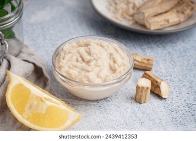 Horseradish sauce in glass bowl with lemon and horseradish roots on white background