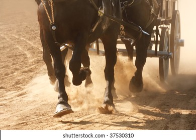 Horses pulling a wagon through a dusty field.