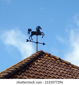 Horse-shaped Weather Vane On Top Of A Roof With Red Tiles.