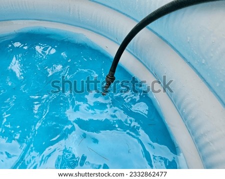 A hose hanging over the side of a pool to fill it with water.