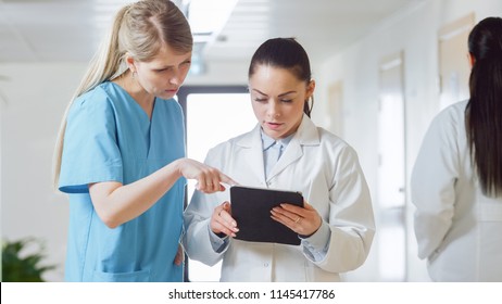 In The Hospital, Busy Doctors Talk, Using Tablet Computer While Standing In The Hallway. New Modern Fully Functional Medical Facility.