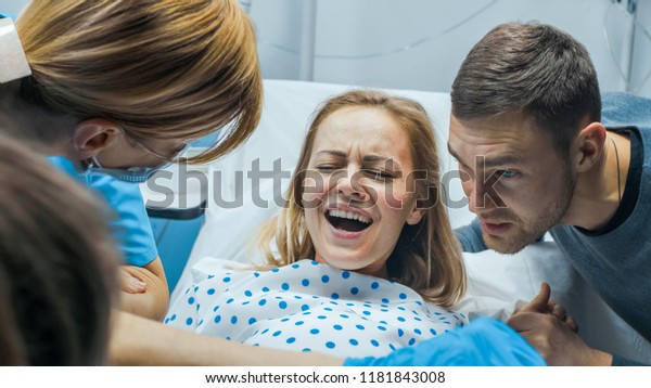 In the Hospital Close-up\
on Woman in Labor Pushes to Give Birth, Obstetricians Assisting,\
Husband Holds Her Hand. Modern Delivery Ward with Professional\
Midwives.
