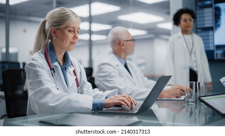 Hospital Conference Meeting Room: Female Physician Works on Laptop Computer Listens to Doctor Presenting Drug Development Data. Team of Medical Research Doctors Discuss Treatment, Medicine, Patients - Powered by Shutterstock