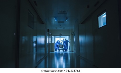 Hospital Emergency Team Carrying Stretcher With Patient Through Dark Hospital Hall.