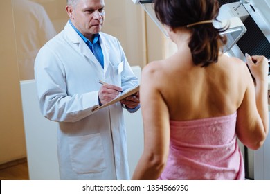 In The Hospital, Female Patient Listens To Mammography Technologist / Doctor Uses Tablet, Explains Importance Of Breast Cancer Prevention. Mammography Procedure.