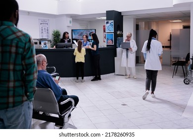 Hospital Front Desk Reception With Mother And Child Filling Form For Doctor Appointment In Private Practice Clinic. Diverse People Waiting In Busy Healthcare Facility For Medical Consultation.