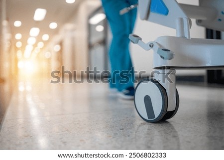 A hospital hallway with a nurse pushing a cart. The hallway is empty and the sun is shining through the windows