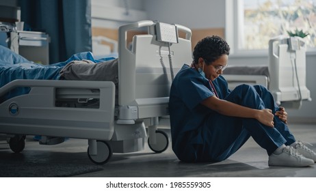 Hospital Intensive Care Coronavirus Ward: Portrait Of Sad, Tired Black Nurse Wearing Face Mask Sitting On A Floor, Sorry For All The Patients Lost To Pandemic. Brave Hero Paramedics Save Lives