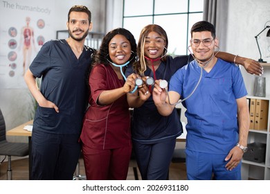 Hospital medical staff in modern room. International doctor team or student group. Mixed race African and Indian Asian doctors showing their stethoscopes to camera and smiling